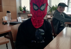 Chłopiec przebrany za Spidermana siedzi przy stoliku w sali lekcyjnej.